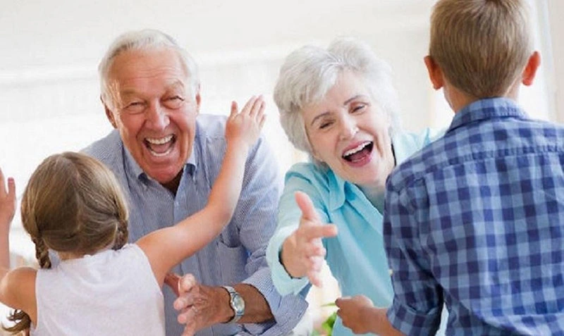 Happy grandparents welcoming two smiling children with open arms in a bright and cheerful home setting.